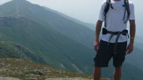 Dan Benson standing on a mountain summit wearing a backpack, with a ridge line in the background