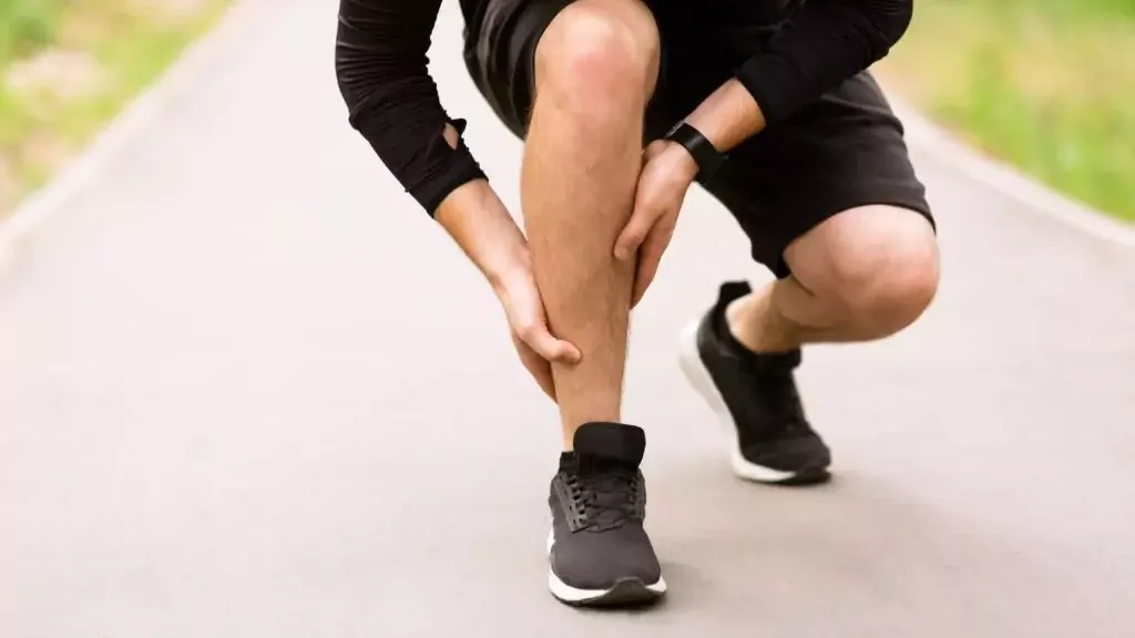 Man gripping his calf in pain while running outdoors on a paved path