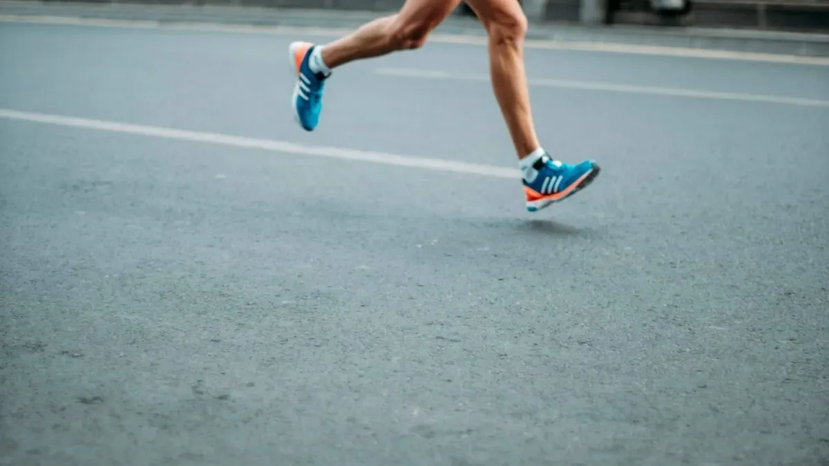 A runner clutching the back of their thigh in pain from a hamstring injury