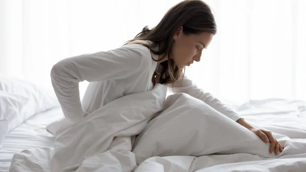 Woman sitting up in bed holding her lower back and hip in discomfort