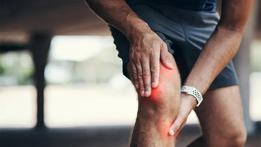 Close-up of a man gripping his knee in pain during outdoor exercise, with a red graphic highlighting the pain area