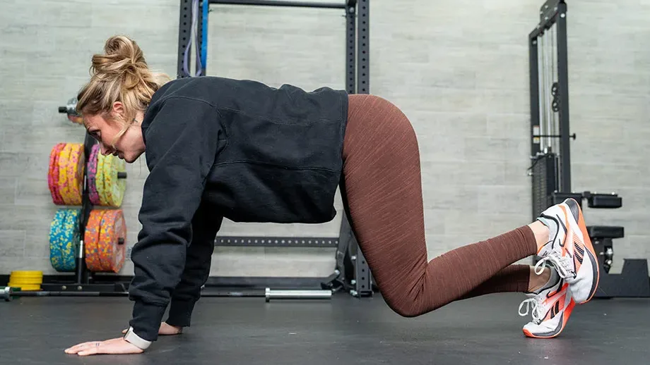 Woman performing a bear hold exercise on all fours in a gym setting