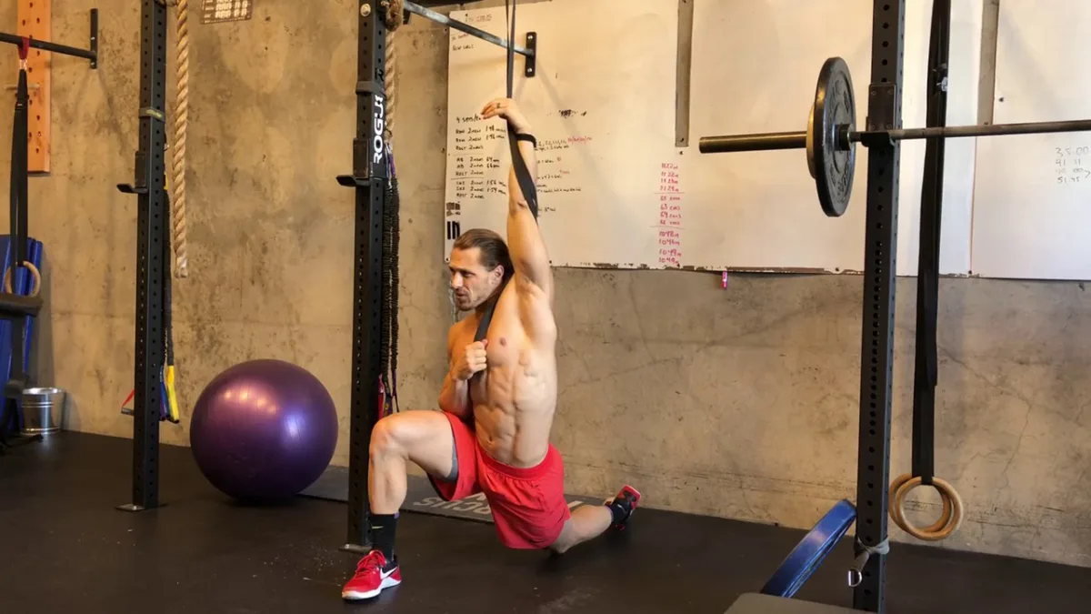 Shirtless man performing a hanging leg raise exercise using a resistance strap in a home gym