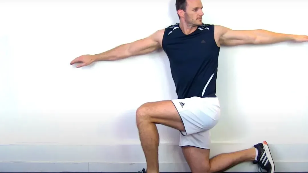 Man performing a standing wall angel stretch with arms extended against a white wall