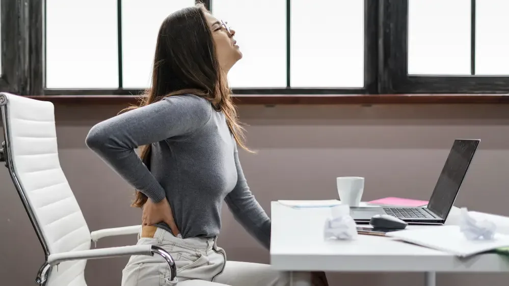 Side view of a woman experiencing back pain while working from home